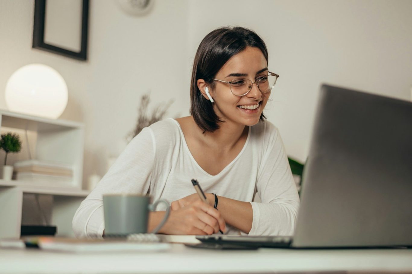 online Supedrvision Lächelnde Frau mit Brille, die an einem Laptop arbeitet und einen Kaffeebecher hält.