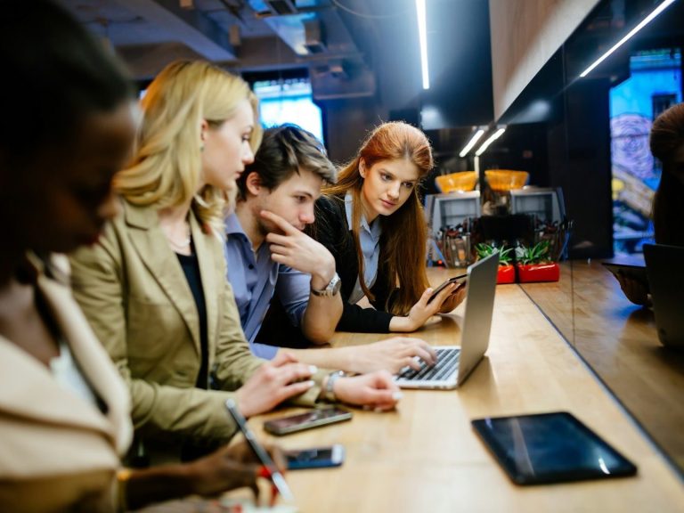 Team Drei Personen arbeiten an Laptops und Smartphones in einem modernen Café.